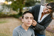 © ByLorena/Stocksy - Mother shaving her teenage son at garden