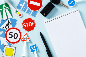 Road traffic signs and blank paper notepad on blue background. Driving school exam concept
