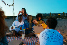 Happy diverse friends eating pizza on beach at evening