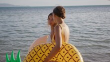 Two Girlfriends Are Walking On The Beach At Sunset Time After Swimming In The Sea With Inflatable Circles. The Women Are Enjoying Their Vacation And Relaxation.