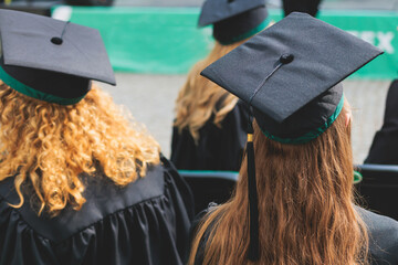 Wall Mural - Graduation ceremony in university, female students wearing black mantles and academic mortarboard cap, group class of high school graduates receive diploma and getting college degree