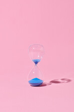 Hourglass With Blue Sand On Pink Background.