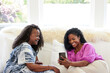 © Trinette Reed/Stocksy - Two Black women friends looking at phone together on sofa at home