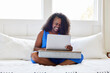 © Trinette Reed/Stocksy - Happy mature Black woman sitting in bed using computer lap desk
