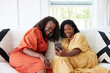 © Trinette Reed/Stocksy - Two mature Black women friends watching phone together on sofa at home