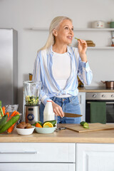 Canvas Print - Mature woman cutting cucumber for healthy smoothie in kitchen