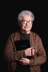 Senior woman with Holy Bible and prayer beads on black background