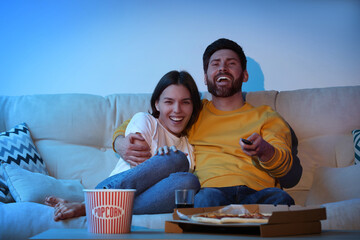 Wall Mural - Happy couple watching TV with popcorn and pizza on sofa