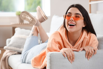 Young woman wearing stylish sunglasses while lying on sofa