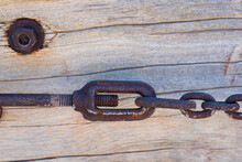 Old Rusty Bolt Locked Tight Pulling On Heavy Duty Iron Chain Links. See Threads On Large Bolt With Old Wood Background.