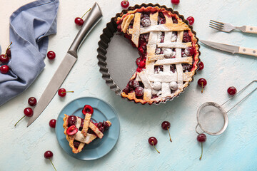 Baking dish with tasty cherry pie and plate of piece on blue background
