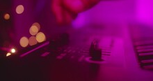 Shakey Close Up Of Hands Of Producer, Musician Turning Sliders And Knobs On Keyboard Dark Recording Studio. 80s Synthwave Hazey Cinematic Purple Aesthetic With Warm Bokeh Lights. Shallow Depth 4K