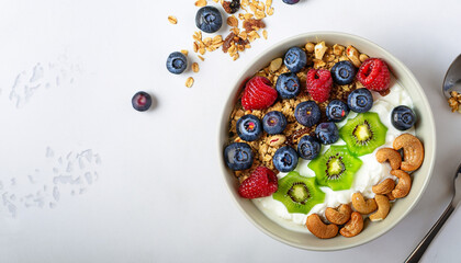 Yogurt bowl with homemade granola (muesli), nuts, fresh berries (blueberry) and kiwi fruit. Healthy eating. Tasty and easy cooking summer breakfast or snack. Top view, copy space, white background.