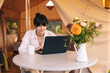 © Ananass - female traveler sitting beside camping tent, drinking morninf coffee and using notebook laptop computer working
