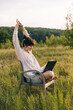 © Ananass - a young woman wearing a shirt works on a laptop while sitting on a chair in the middle of nature
