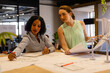 Diverse female architects in discussion using blueprints in casual office meeting