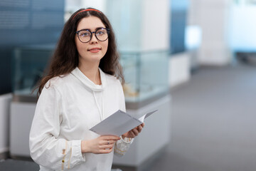 Wall Mural - Portrait of pretty young caucasian girl student wearing eyeglasses visiting museum exhibition. Light hall in background. Concept of cultural education and Museum's Day