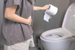 Close-up a woman putting hand on her stomach and holding a roll of toilet paper as she goes to the toilet to poop. Woman has a stomach ache. A woman going to the toilet needs excretion in the morning.
