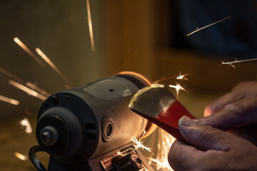 man sharpening an ax on a lathe, sparks fly