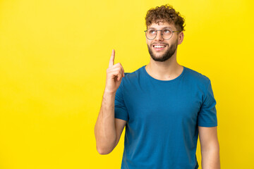 Canvas Print - Young handsome caucasian man isolated on yellow background pointing up and surprised