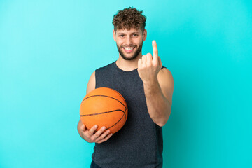 Canvas Print - Handsome young man playing basketball isolated on blue background doing coming gesture