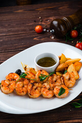 Wall Mural - Fried shrimp on a skewer with rustic potatoes, lemon, tomatoes, olives and sauce, fresh dinner.