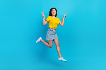 Wall Mural - Full length photo of nice cheerful girl good mood dressed yellow t-shirt denim skirt show v-sign flying isolated on blue color background