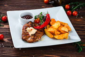 Poster - Fried pork fillet steak with Rustic fried potato wedges, onions, chili peppers, cherry tomatoes and sauce in a plate.