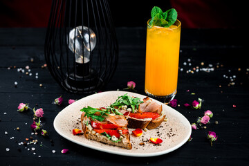 Canvas Print - Bruschetta with bacon slices, sweet pepper, blue cheese, arugula in a plate and orange lemonade.