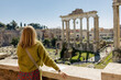 A happy blond woman tourist is standing near the Roman Forum, old ruins at the center of Rome, Italy. Concept of traveling famous landmarks.