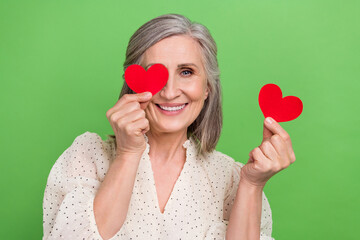 Sticker - Photo portrait of beautiful grandma hold two little heart cards cover face dressed stylish white garment isolated on green color background