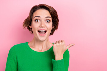 Portrait of young surprised woman wear green trendy pullover direct thumb mockup demonstrate wish list isolated on pink color background