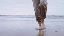 Person Walking On The Ocean Coast Beach, Woman's Feet On Sand Slowly Approaching Camera In Moody Weather After Sunset, Cinematic Gimbal Shot