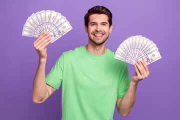 Sticker - Portrait of positive good mood guy with bristle wear green t-shirt two arms hold dollars win lottery isolated on violet color background