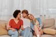 modern family, polygamy concept, freedom in relationship, cultural diversity, redhead man sitting with multicultural women on couch in living room, polyamorous lifestyle, non traditional