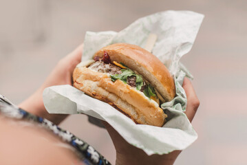 Unrecognizable woman eats burger outdoor closeup. Street cafe. Young woman eating fast food with appetite. Girl eating with great pleasure, woman eating burger, food. No face hands closeup