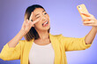 © Sharne T/peopleimages.com - Asian woman, peace sign and funny face for selfie, photo or memory against a purple studio background. Happy female person or model pose with peaceful emoji, goofy or silly for picture or online vlog