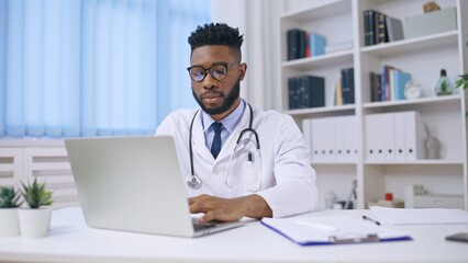 African American male doctor working on laptop in office, online consultation services, healthcare