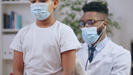 Wall Mural - Pediatrician examining sick boy in medical face mask to diagnose disease