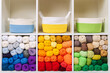 Shelving with storage baskets and colored balls of yarn for knitting. Bright yarn balls lined up on the shelves. Organizing and storage in craft room. Handmade, needle craft, creativity and  hobby.