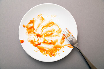 Dirty white ceramic plate with tomato sauce stains, food leftovers and fork, top view