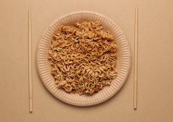 Instant noodles in cardboard plate with chopsticks on beige background. Top view