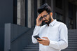 © Liubomir - Young hispanic businessman outside office building, man in shirt reading sad bad news online using app on phone, depressed man disappointed unhappy with achievement results.