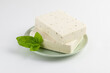 Two pieces of tofu, paneer or soy cheese with fresh basil leaves in a green plate isolated on white