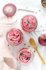 Jars of freshly prepared sliced pickled red onions on a white cutting board.