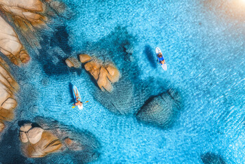 Sticker - Aerial view of sup boards, blue sea, rocks at sunrise in summer. People on floating canoe in transparent azure water. Kayak. Sardinia island, Italy. Tropical seascape. Active travel. Top drone view