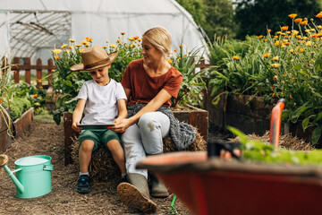 Mother is sitting on a hayrick with er son in the garden. They are looking at digital tablet.