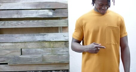 Wall Mural - Happy african american man wearing yellow t shirt pointing to pocket, slow motion, copy space