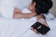 Young man is sleeping on the bed with the phone still in h is hand while the alarm ringing. Oversleeping concept. Selective focus