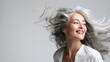 Smiling mature woman with silvery, grey hair in front of a white background in a profile position and wind blowing, portrait with generative ai